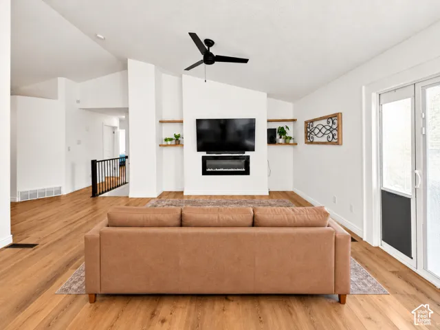Vaulted ceilings, wood-finish flooring, built-in electric fireplace, recessed lighting, and a black ceiling fan
