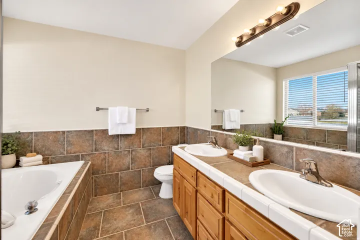 Dual vanity with wood-finish cabinetry, tile countertop, and integrated sinks