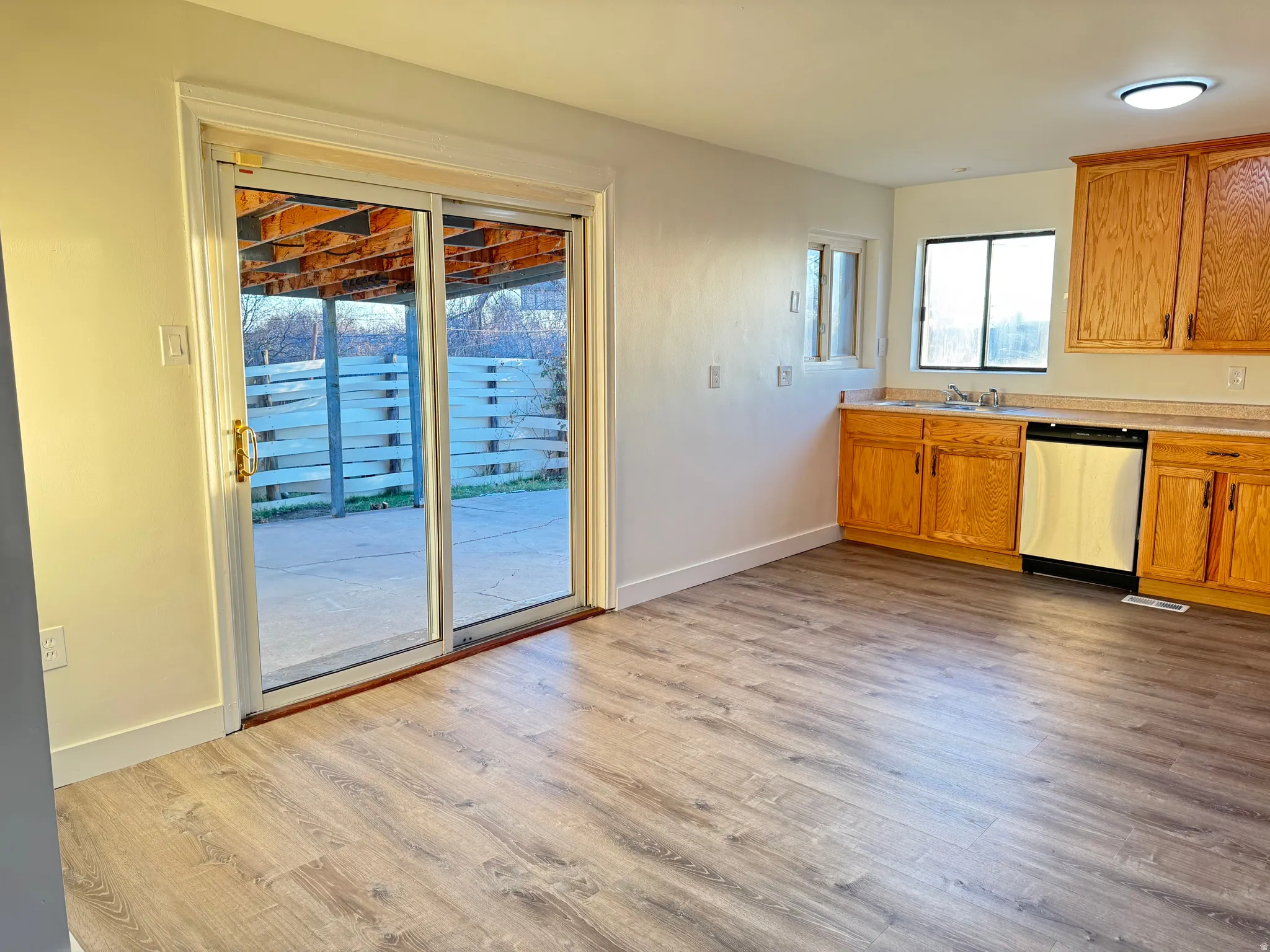 Kitchen featuring light countertops, stainless steel dishwasher, light wood finished floors, and brown cabinetry