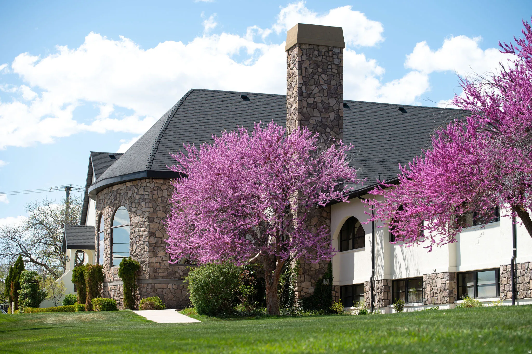 View of front of home featuring stone siding, roof with shingles, a front yard, stucco siding, and a chimney