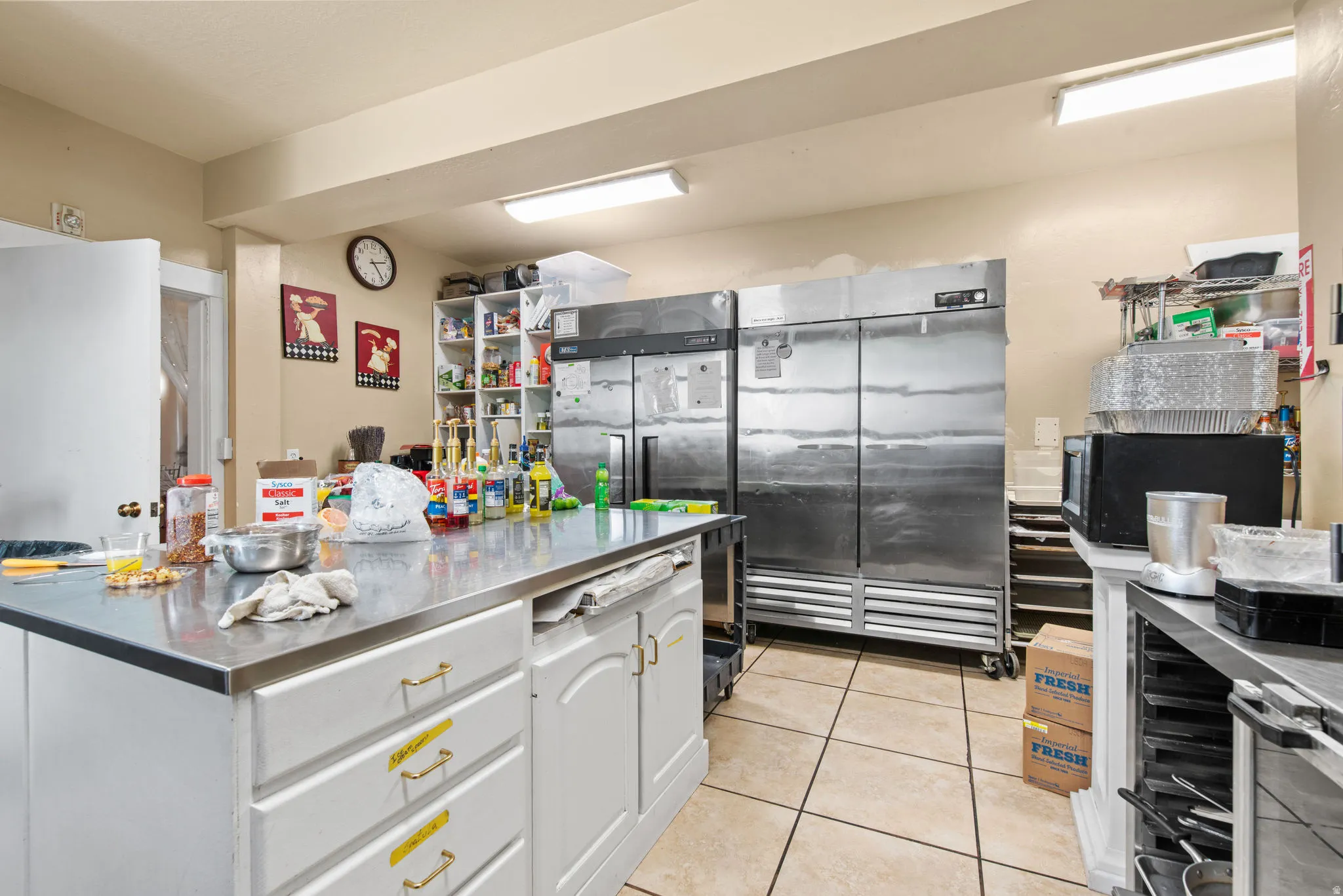 Kitchen with stainless steel countertops, white cabinets, stainless steel fridge, light tile patterned flooring, and black microwave