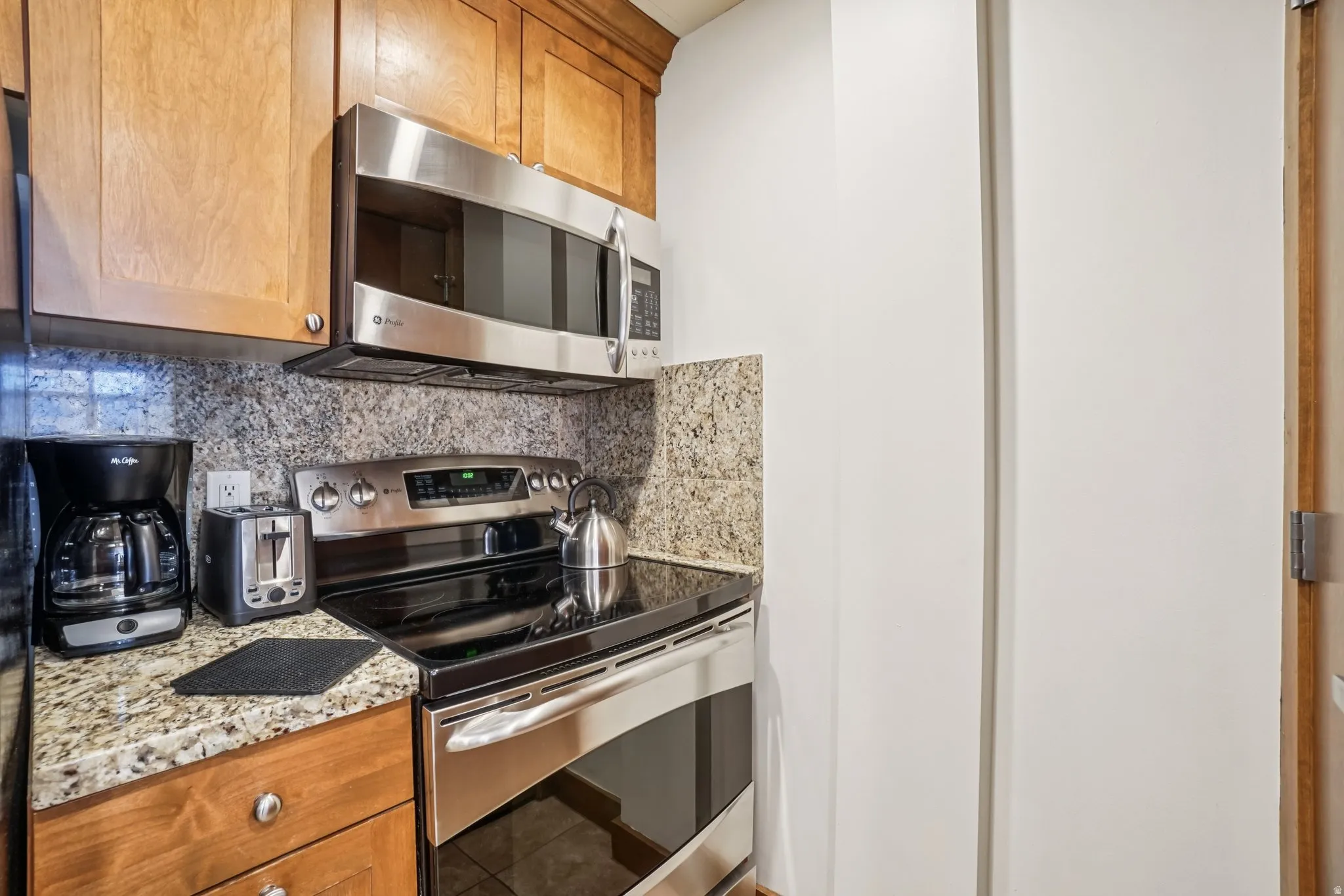 Kitchen with appliances with stainless steel finishes, backsplash, brown cabinets, and light stone counters