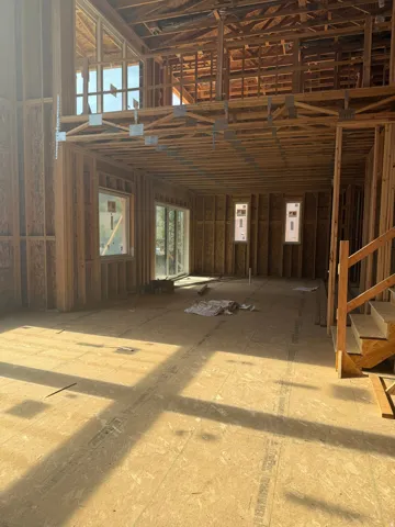 Open-concept interior featuring exposed wood-beam ceiling structure, abundant natural light from multiple windows, concrete subfloor, and framed interior walls ready for finishing