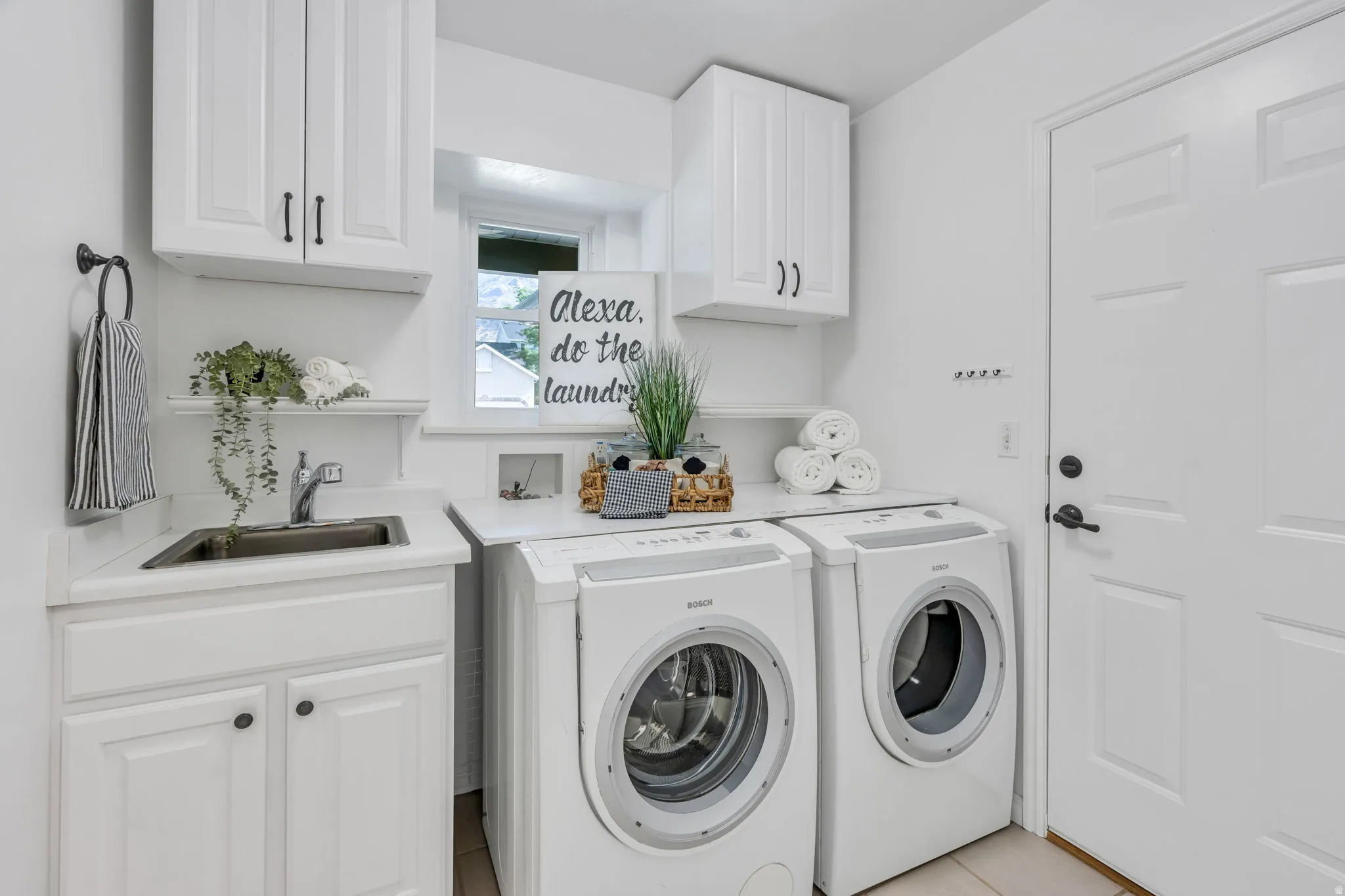 Laundry room featuring overhead white cabinetry, integrated utility sink, and a window for natural light