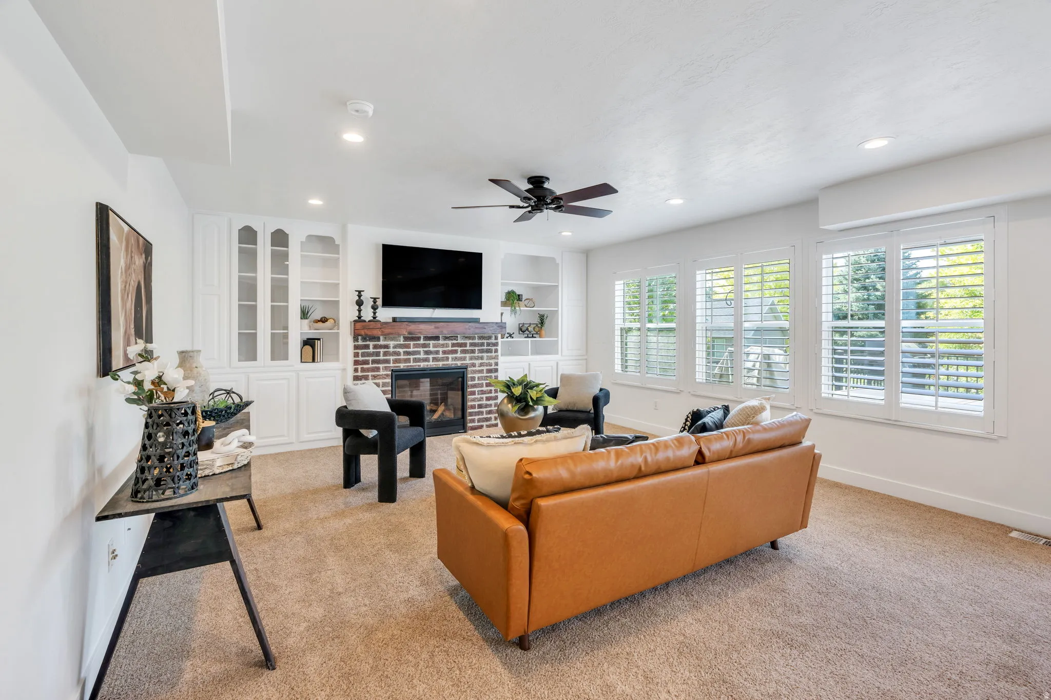 Living area featuring a brick fireplace with a wood-beam mantel, flanked by custom built-in cabinetry with glass-front doors