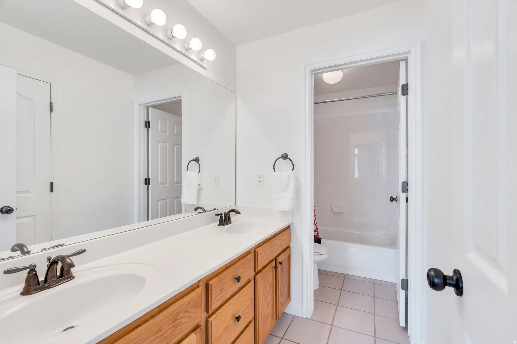 Hall way bathroom with double sinks and door to tub/shower, toilet area