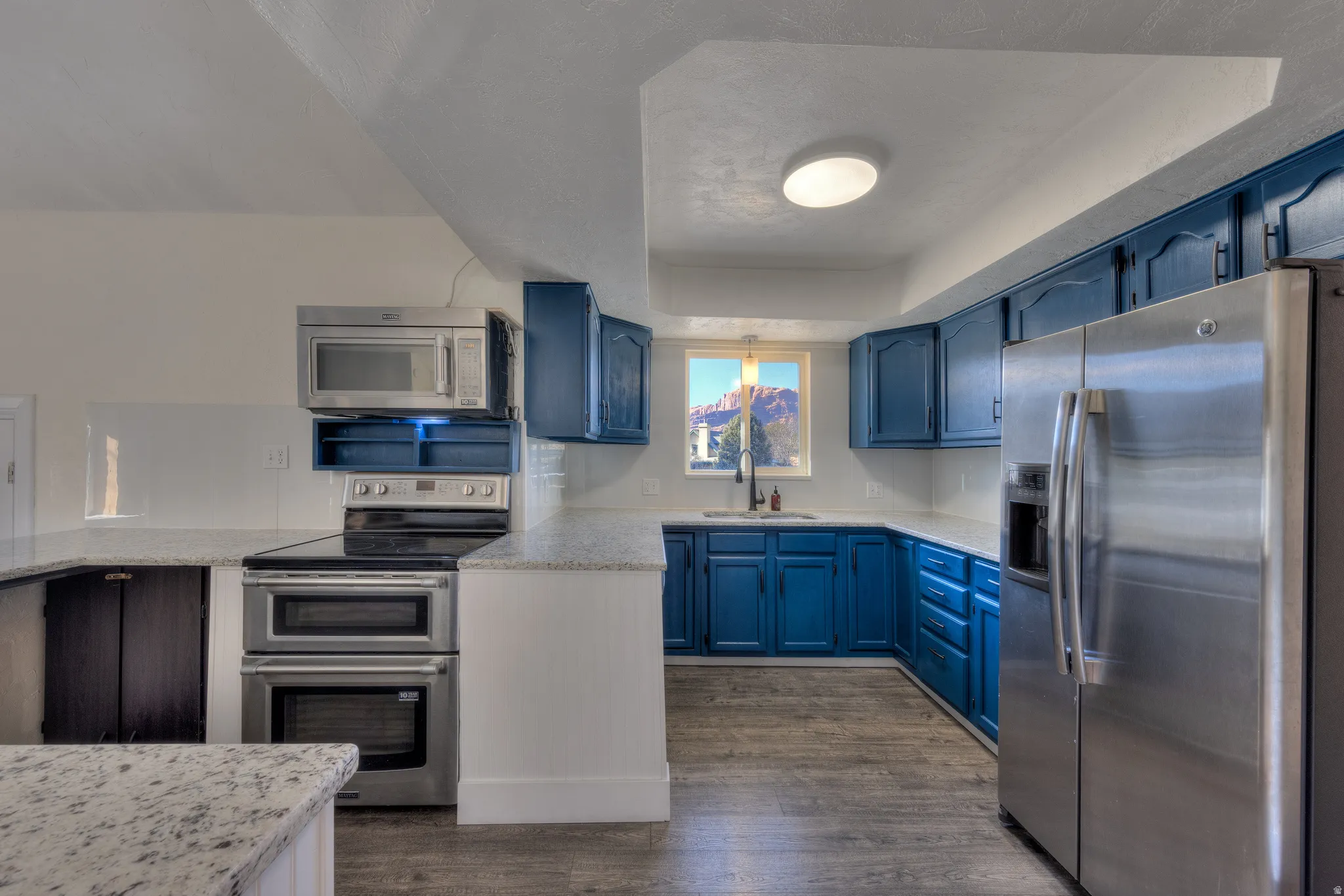 Kitchen with stainless steel appliances, a raised ceiling, classy blue cabinetry, light granite counters, and LVP floors