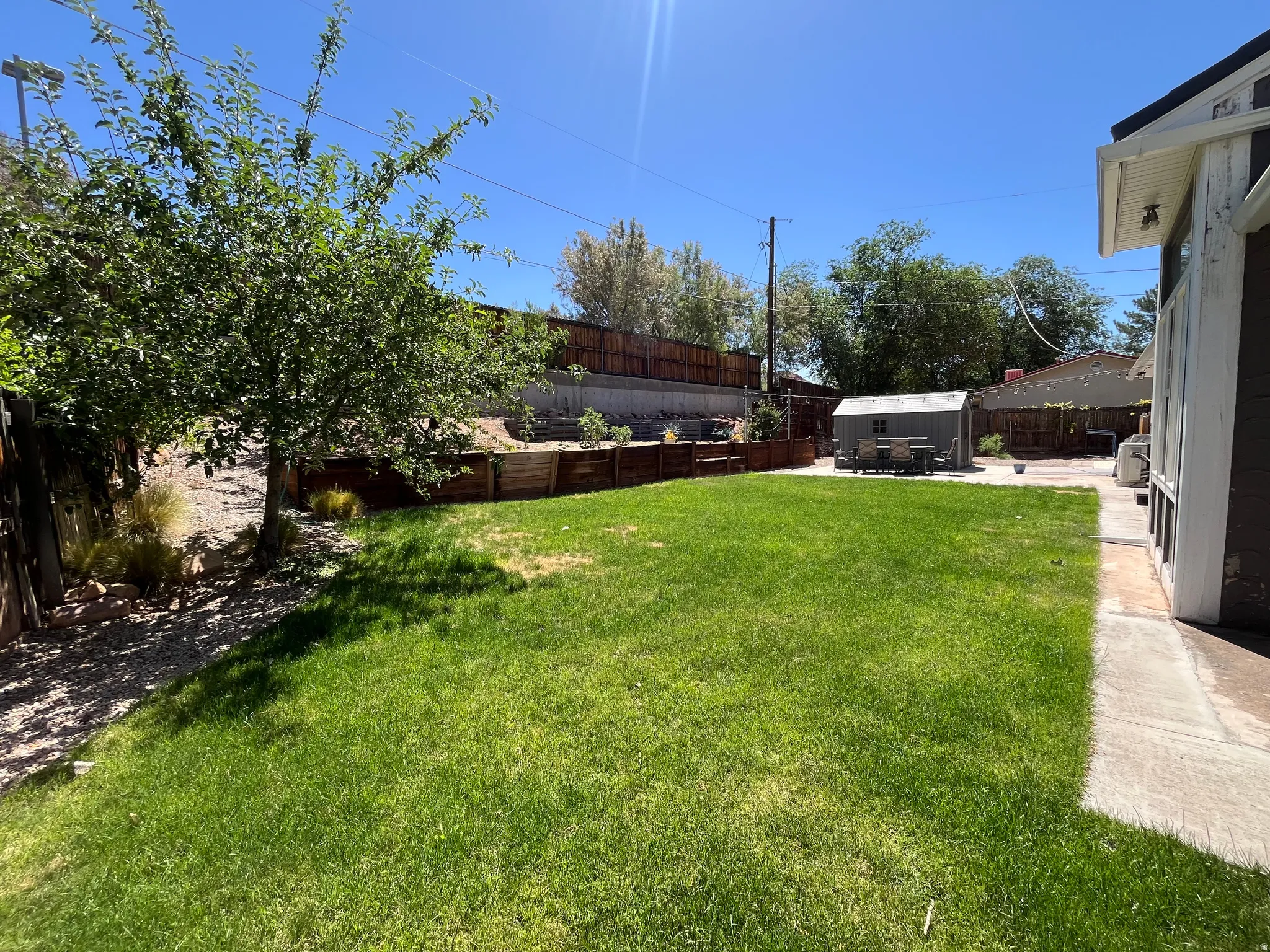 Spacious backyard featuring a manicured lawn, a concrete patio, and a storage shed