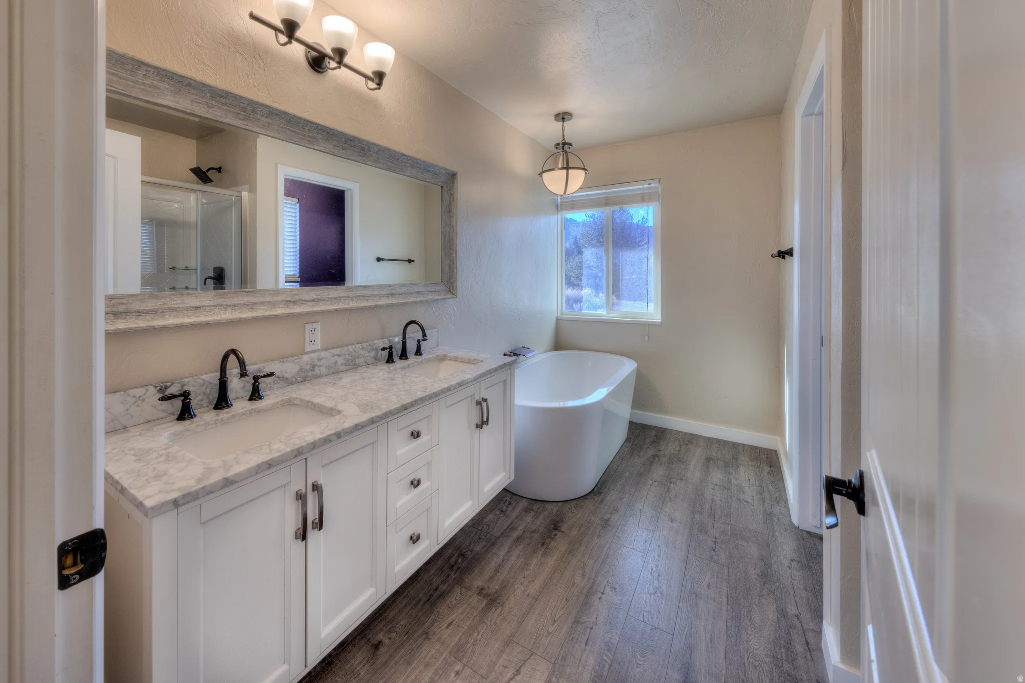 Full bath with double vanity, LVP flooring, a freestanding tub, and a seperate shower