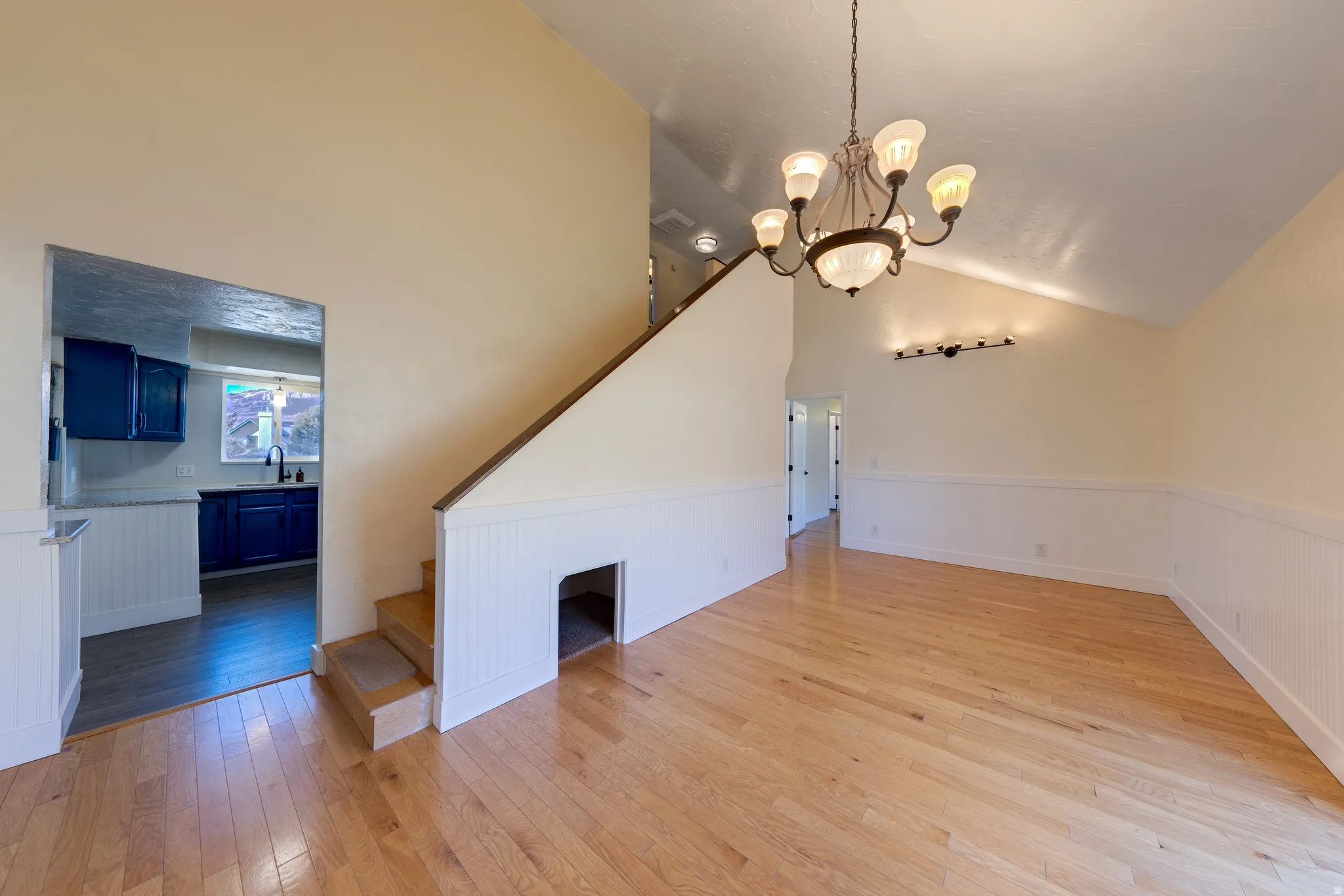 Living room with a wainscoted wall, light oak flooring, stairway, a chandelier, and lofted ceiling