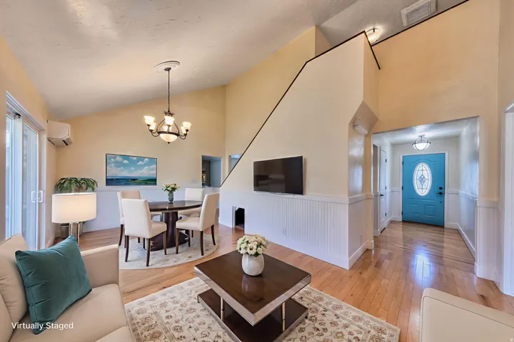 Living area with wainscoting, light oak flooring, a chandelier, high vaulted ceiling, and an AC wall unit