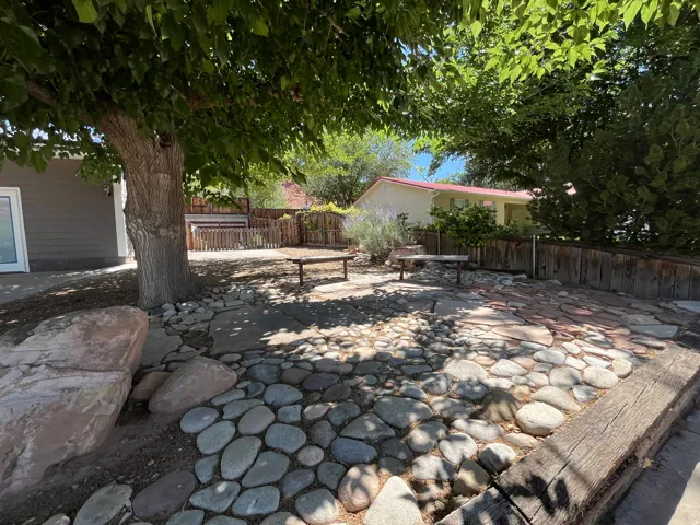 Outdoor patio featuring a stone and paver surface, bordered by a wooden retaining wall and a wood privacy fence