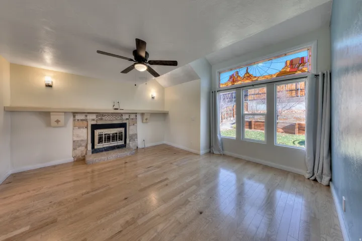Unfurnished living room featuring oak floors, a stone fireplace, ceiling fan, and vaulted ceiling