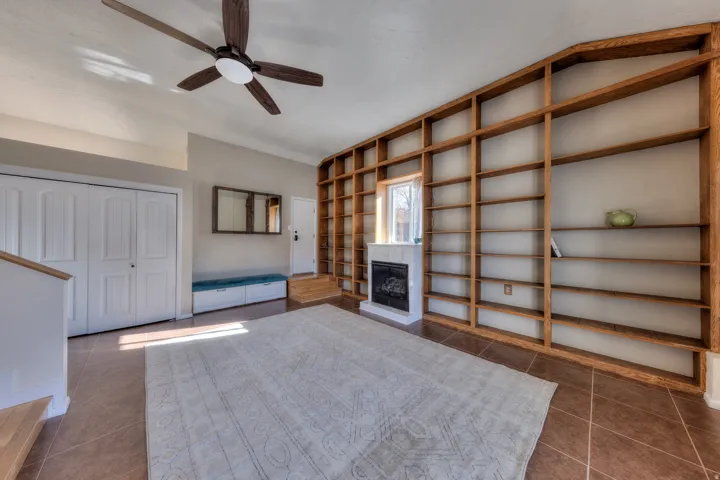 Great room featuring built in bookcases, a fireplace with raised hearth, ceiling fan, tile flooring, and vaulted ceiling