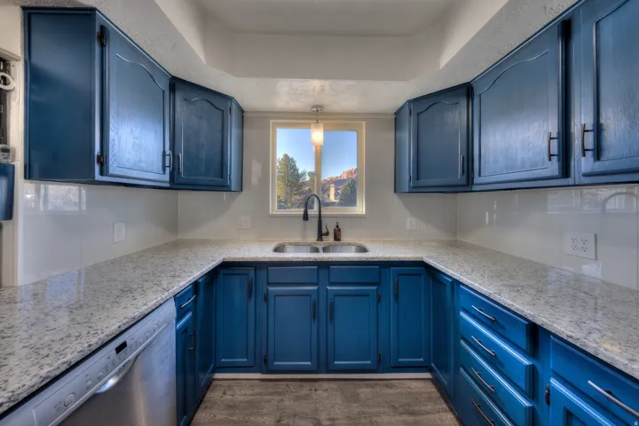 Kitchen featuring classy blue cabinets, stainless steel dishwasher, light granite counters, and pendant lighting