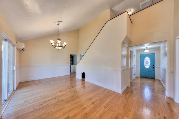 Entryway with wainscoting, light oak flooring, vaulted ceiling, a chandelier, and an AC wall unit