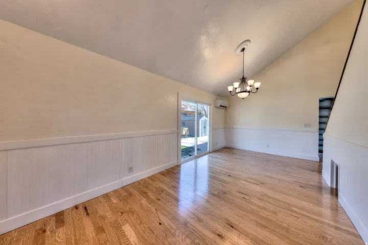 Dining area with lofted ceiling, wainscoting, light oak floors, and chandelier