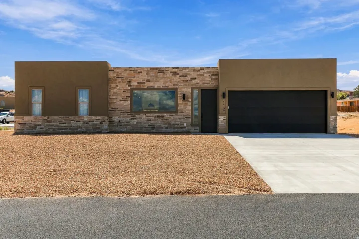 Stucco and stone facade with a modern black garage door, a concrete driveway, and a gravel front yard