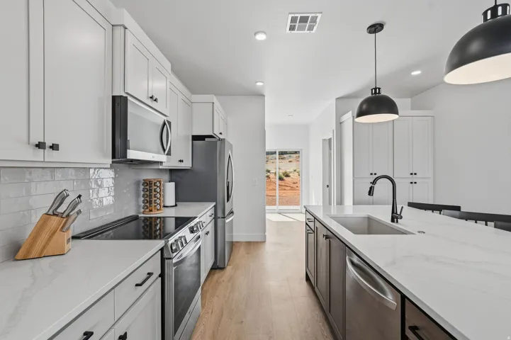 Modern kitchen featuring stainless steel appliances, white flat-panel cabinetry, white subway tile backsplash, and light wood-finish flooring