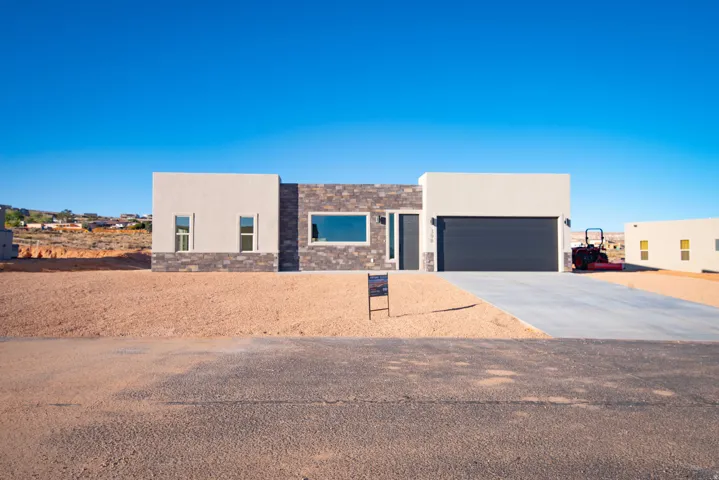 View of front of house with concrete driveway, stucco siding, stone siding, and an attached garage