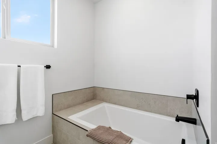 Built-in soaking tub with matte black fixtures, integrated tile surround, and an overhead window