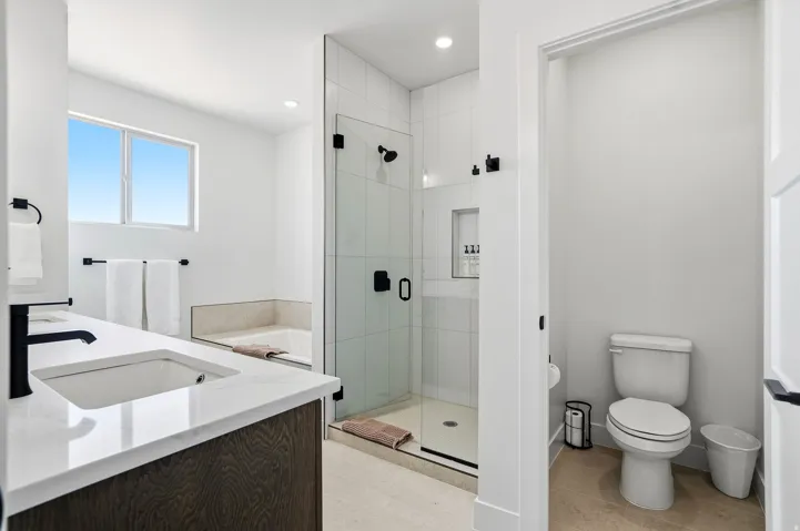 Modern bathroom featuring a wood-finish vanity with a single sink and white countertop, walk-in shower with clear glass enclosure and subway tile, and a built-in soaking tub
