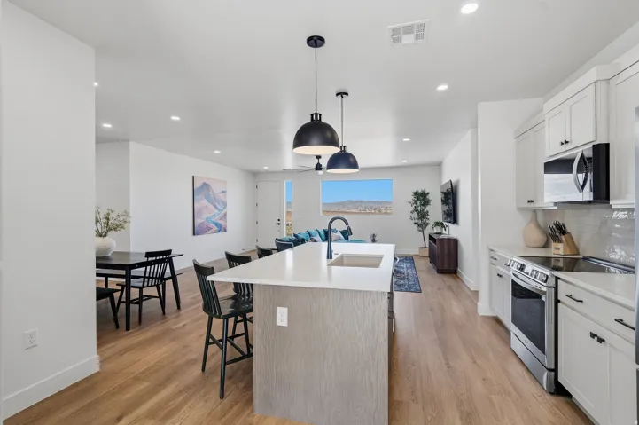 Open-concept living space featuring wood-finish flooring, a kitchen island with integrated sink, stainless steel appliances, and white cabinetry