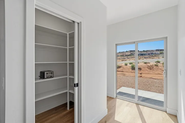 Sliding glass door with an exterior concrete pad, wood-finish flooring, and a pantry with built-in shelving