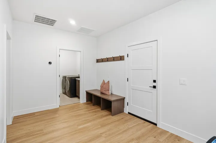 Wood-finish flooring, white paneled door with black hardware, wall-mounted coat rack, and recessed lighting
