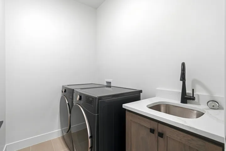 Laundry area featuring wood-finish cabinetry, a stainless steel sink, a matte black faucet, and light countertops