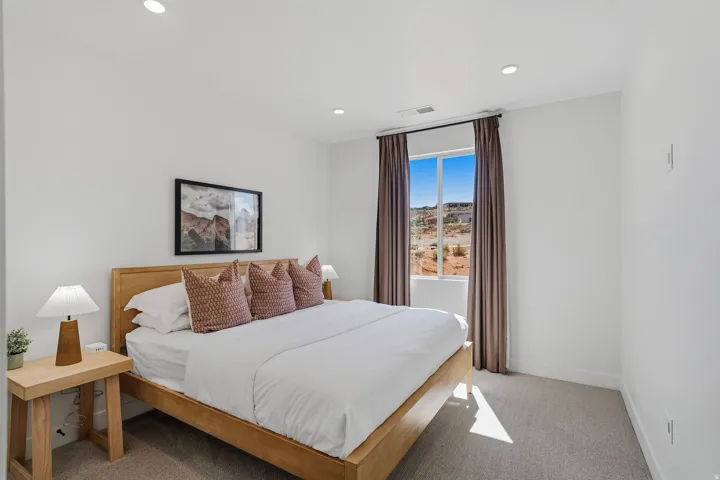 Recessed lighting illuminates a space featuring light-toned carpeting and a window with dark curtain panels