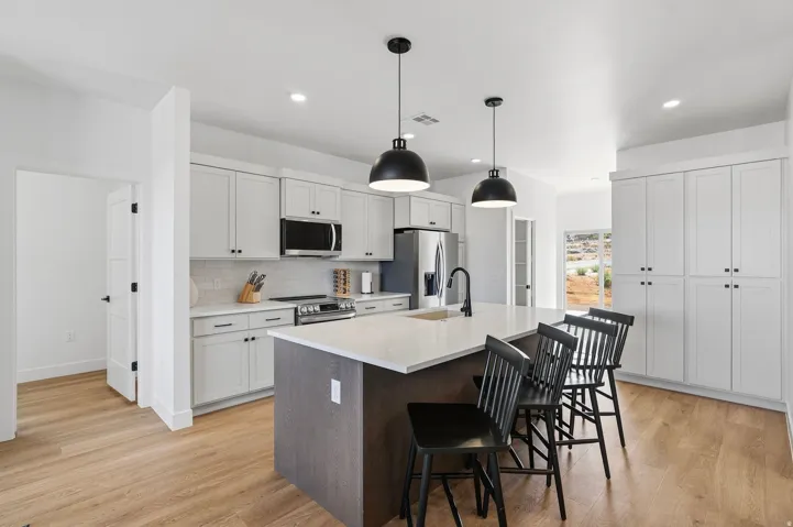 Modern kitchen featuring light wood-finish flooring, white cabinetry, integrated stainless steel appliances, a center island with pendant lighting, and a white countertop