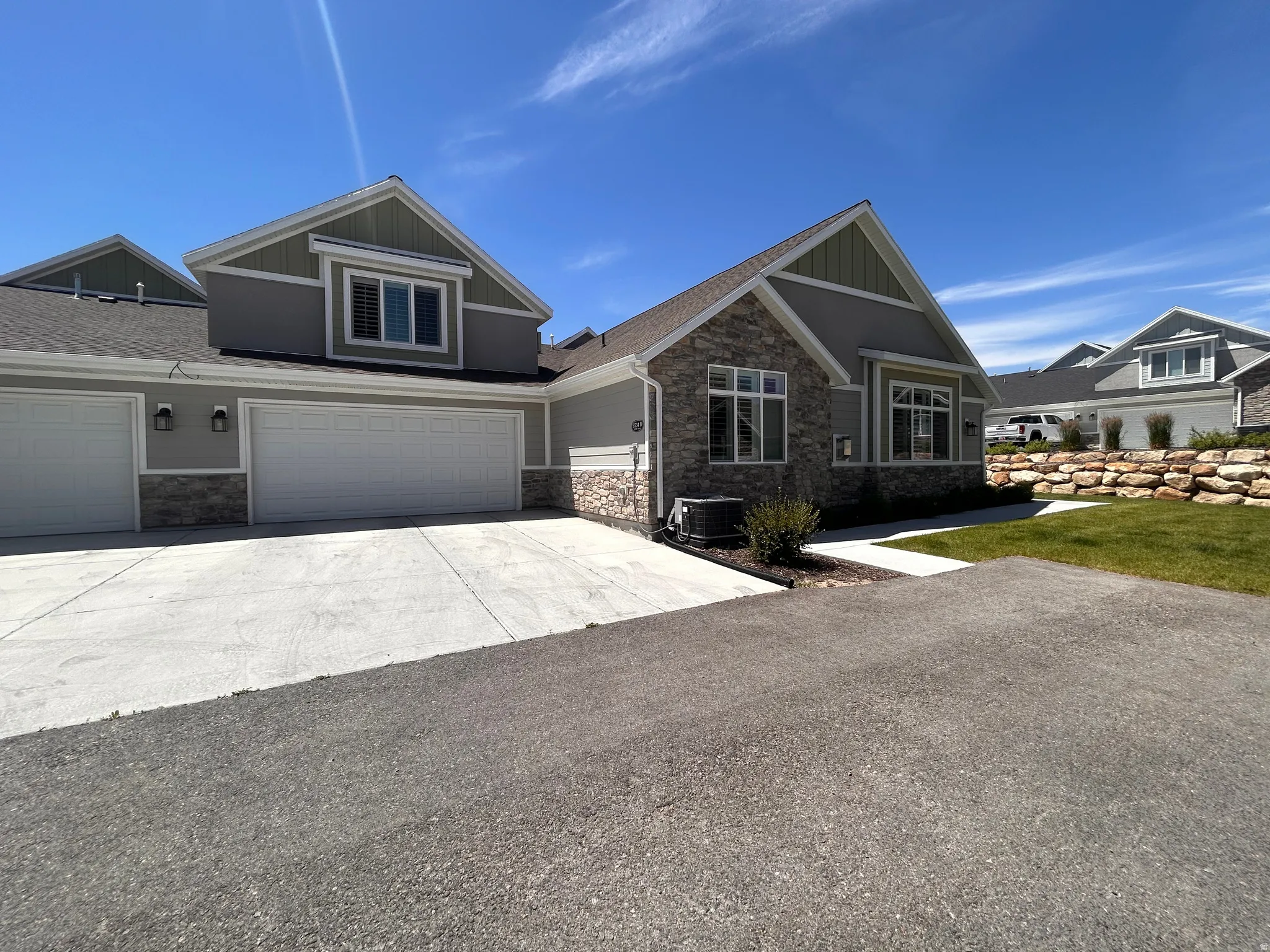 Modern townhome exterior featuring a stone and siding facade, multiple garage doors, and a well-maintained lawn