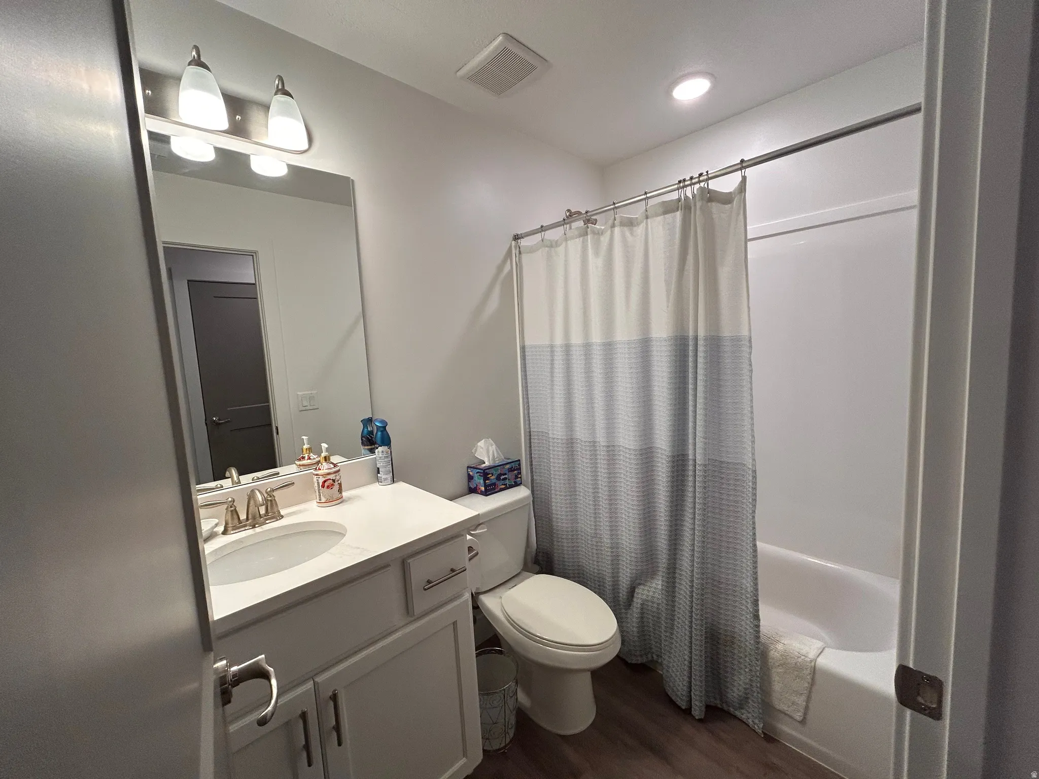 Full bath with shower / bathtub combination with curtain, vanity, and dark wood-style floors
