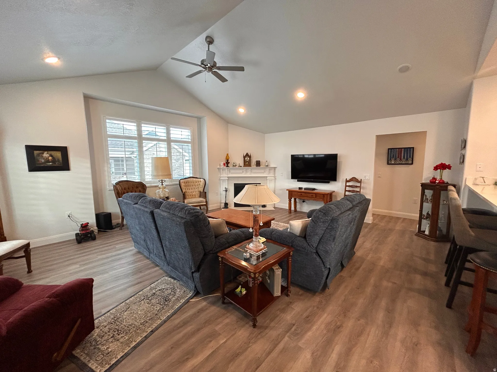 Living room with vaulted ceiling, a fireplace, wood finished floors, a ceiling fan, and recessed lighting