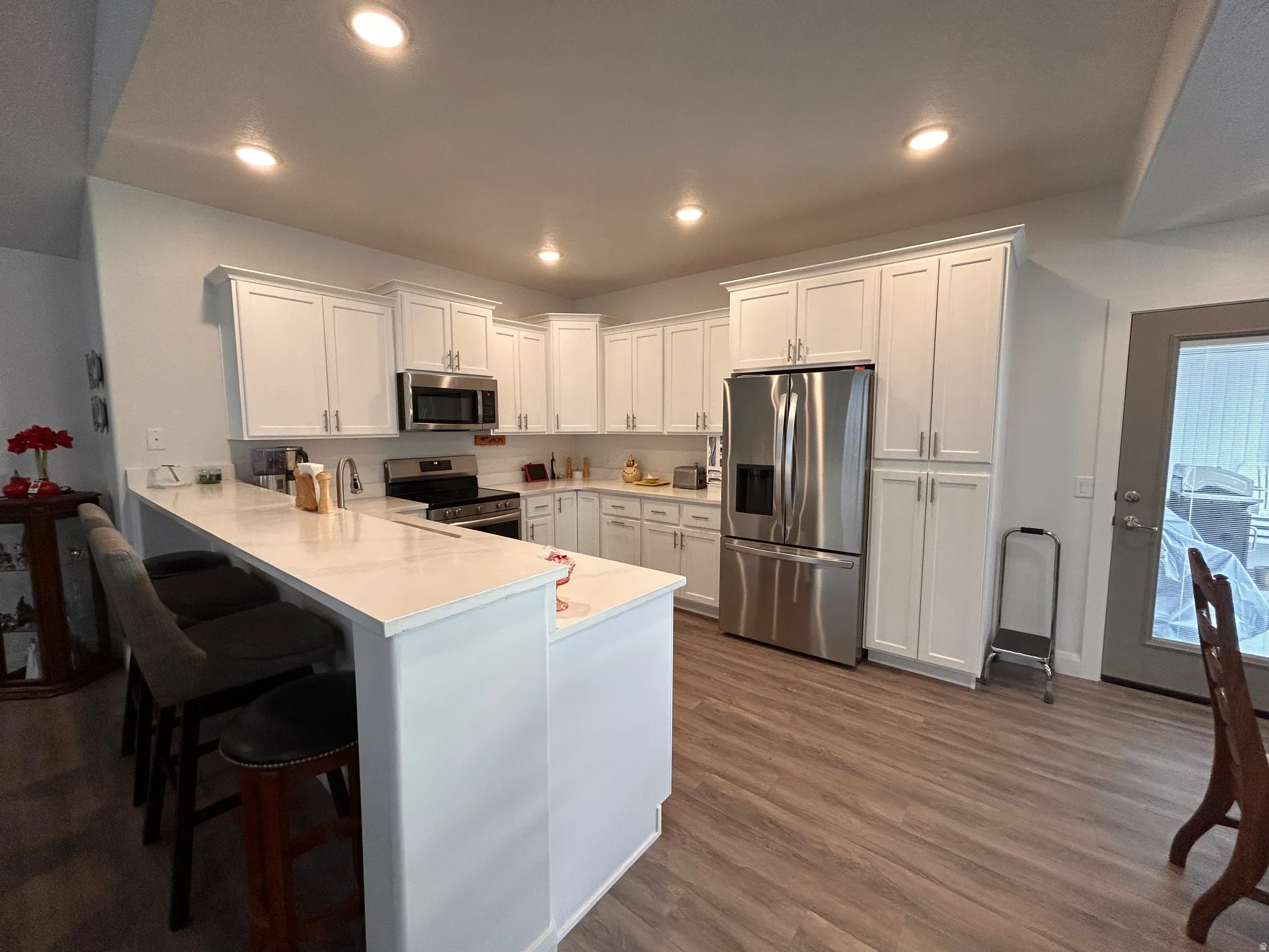 Kitchen with appliances with stainless steel finishes, white cabinets, a kitchen breakfast bar, a peninsula, and recessed lighting
