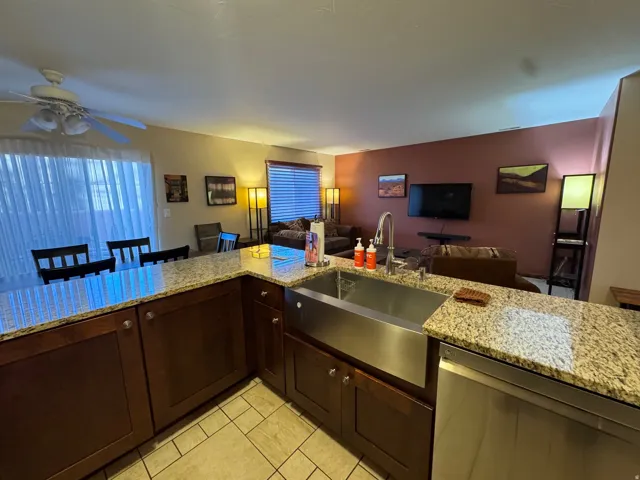 Kitchen with dark brown cabinets, light stone counters, dishwasher, open floor plan, and ceiling fan