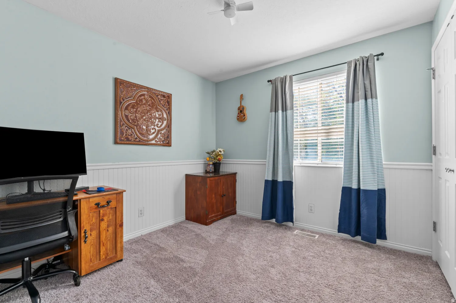 Office space with light carpet, ceiling fan, and a wainscoted wall