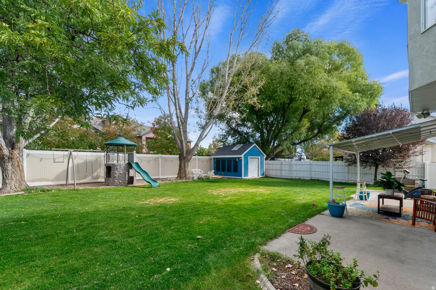 Fenced backyard with an outbuilding, a playground, and a patio