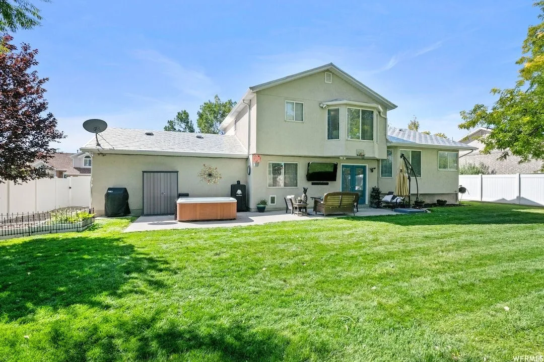 Rear view of property with a hot tub, a fenced backyard, a patio area, and stucco siding
