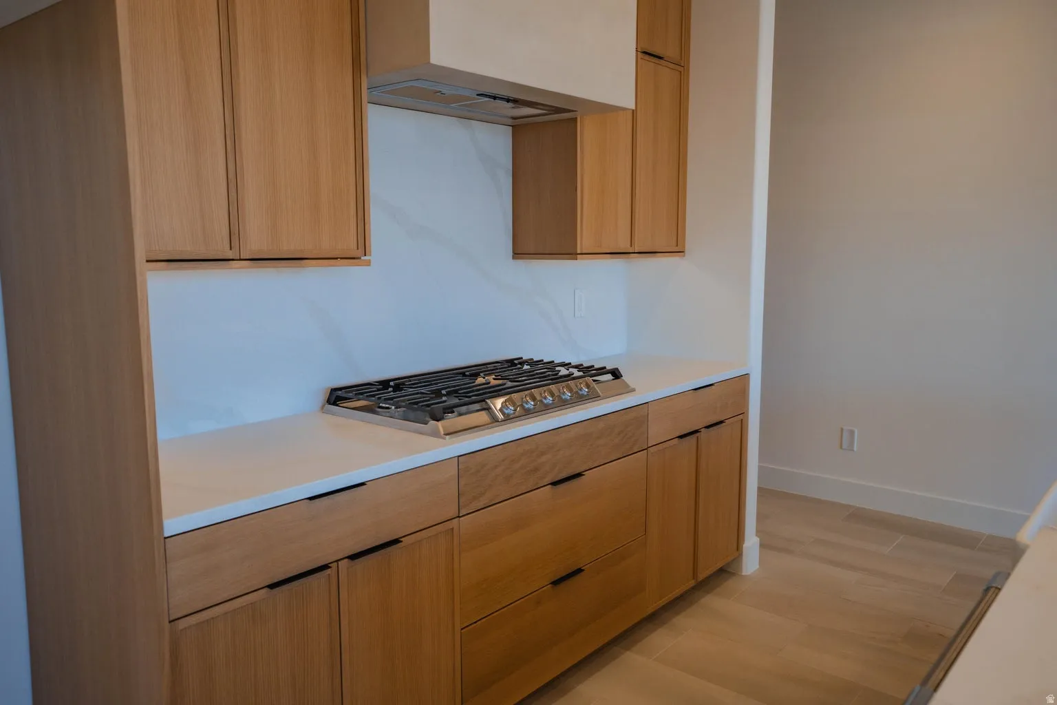 Kitchen featuring light wood-type flooring, stainless steel gas stovetop, premium range hood, light stone counters, and modern cabinets