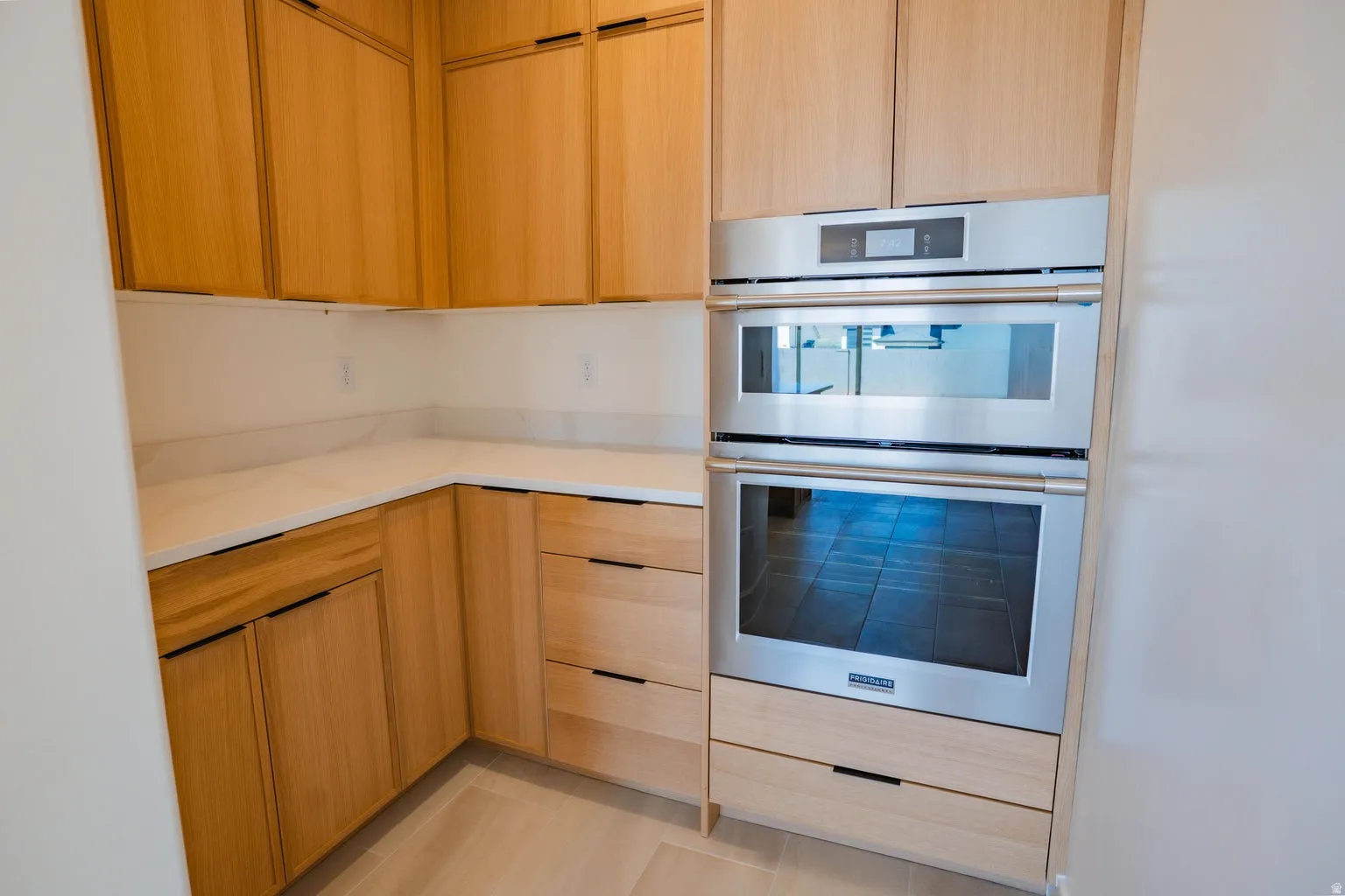 Kitchen with modern cabinets, stainless steel double oven, light brown cabinets, light stone countertops, and light tile patterned flooring