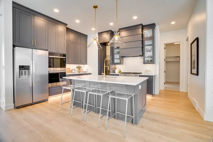 Kitchen with gray cabinetry, a breakfast bar area, decorative light fixtures, a kitchen island with sink, and appliances with stainless steel finishes