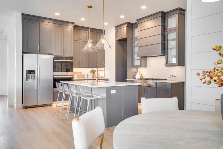 Kitchen with gray cabinetry, stainless steel appliances, decorative light fixtures, light stone counters, and recessed lighting