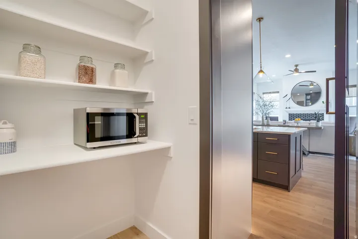 Kitchen featuring stainless steel microwave, light wood-style floors, hanging light fixtures, open shelves, and ceiling fan