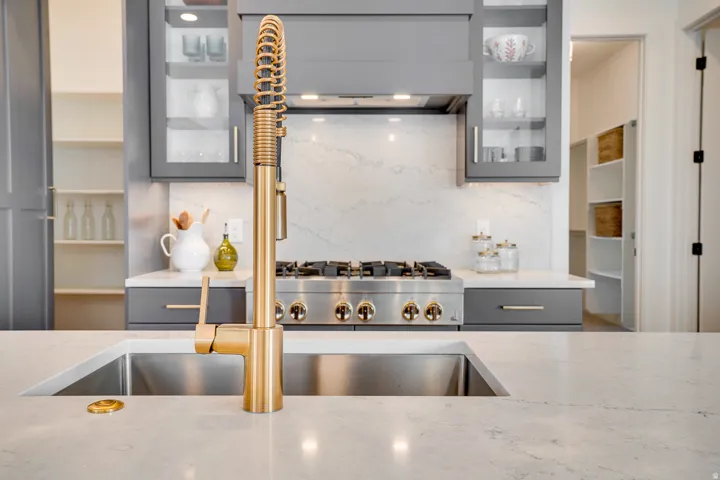 Kitchen featuring gray cabinets, light stone counters, backsplash, and glass insert cabinets