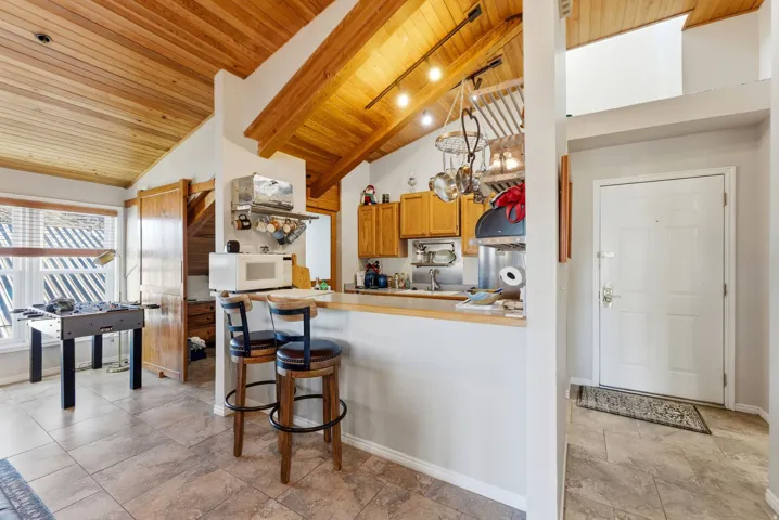 Kitchen featuring wooden ceiling, a kitchen bar, white microwave, light countertops, and brown cabinetry