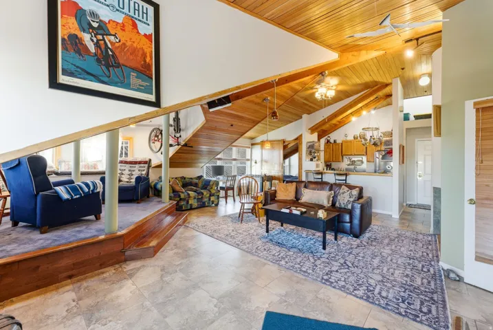 Living room featuring wooden ceiling, high vaulted ceiling, a ceiling fan, and stone tile floors