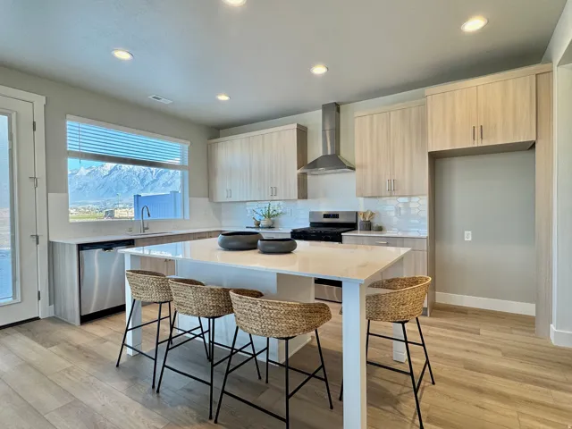Kitchen featuring modern cabinets, light stone countertops, a kitchen bar, wall chimney exhaust hood, and stainless steel appliances