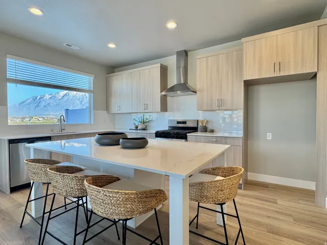 Kitchen with light stone countertops, modern cabinets, wall chimney exhaust hood, a kitchen bar, and stainless steel appliances